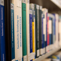 Foto: Ein Bücherregal in einer Bibliothek mit verschiedenen Büchern. Ein Buch trägt den Titel 'Ganzheitliche Gestaltung von Investmentprozessen'.