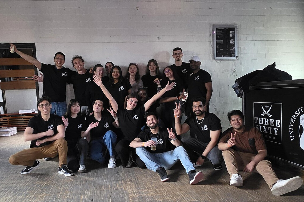 Foto: Eine Gruppe von Personen steht und sitzt in einem Raum. Sie tragen schwarze T-Shirts mit einem Logo. Im Hintergrund ist ein Tresen mit den Logos von 'Three Sixty Vodka' und 'Universität Hohenheim' zu sehen.