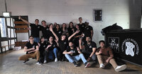 Foto: Eine Gruppe von Personen steht und sitzt in einem Raum. Sie tragen schwarze T-Shirts mit einem Logo. Im Hintergrund ist ein Tresen mit den Logos von 'Three Sixty Vodka' und 'Universität Hohenheim' zu sehen.