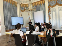 Foto: Eine Gruppe von Personen sitzt in einem dekorativen Raum und hört einem Vortrag über Risikobewertung zu. Auf einem Bildschirm ist der Titel 'CASE STUDY - RISK ASSESSMENT' zu sehen.