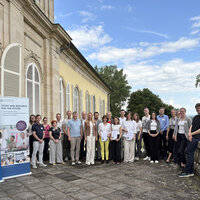 Foto: Eine Gruppe von Personen steht vor einem historischen Gebäude der Universität Hohenheim. Neben ihnen sind Banner mit der Aufschrift 'Universität Hohenheim' und 'Study and Research for the Future' zu sehen.
