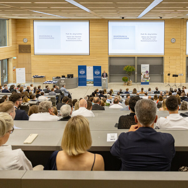 Foto: Ein Hörsaal der Universität Hohenheim ist gefüllt mit Personen, die einer Präsentation von Prof. Dr. Jörg Schiller zuhören. Auf der Leinwand steht 'Begrüßung & Danksagungen'.