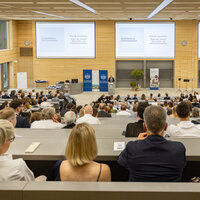 Foto: Ein Hörsaal der Universität Hohenheim ist gefüllt mit Personen, die einer Präsentation von Prof. Dr. Jörg Schiller zuhören. Auf der Leinwand steht 'Begrüßung & Danksagungen'.