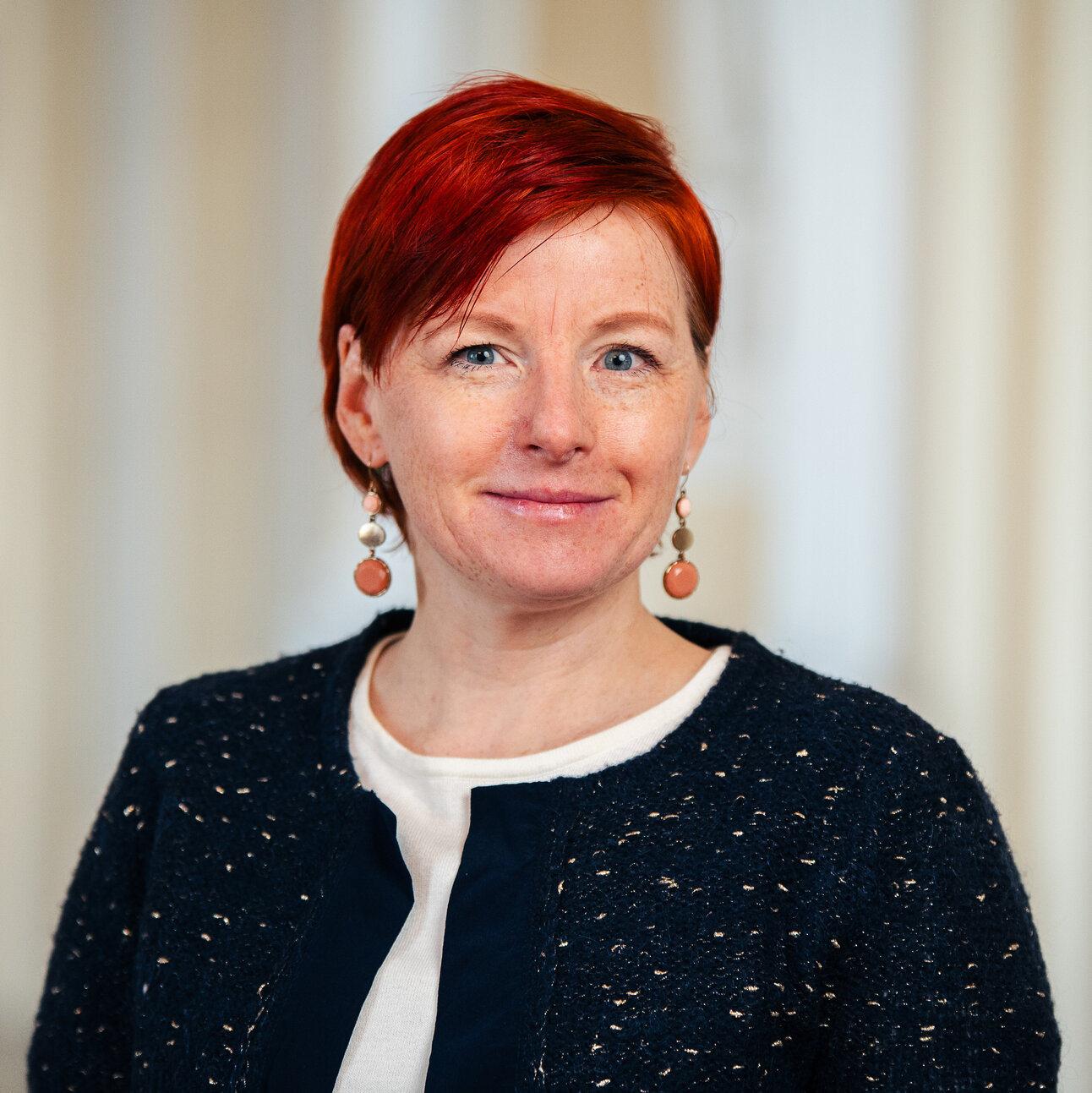 Foto: Eine Person trägt einen dunkelblauen Blazer mit weißen und blauen Details und steht vor einem unscharfen Hintergrund.