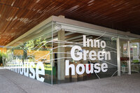 Foto: Das Inno Greenhouse der Universität Hohenheim mit großen Glaswänden und der Aufschrift 'Inno Greenhouse'. Im Inneren sind Pflanzen und Möbel sichtbar.