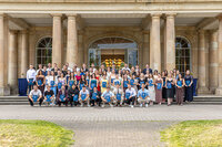 Foto: Eine Gruppe von Personen steht vor Schloss Hohenheim. Sie halten Zertifikate und posieren für ein Foto. Das Gebäude im Hintergrund hat Säulen und große Fenster.