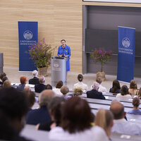 Foto: Eine Person hält einen Vortrag im Hörsaal der Universität Hohenheim. Im Hintergrund sind zwei Banner mit dem Logo der Universität sichtbar. Das Publikum sitzt in Reihen und hört zu.