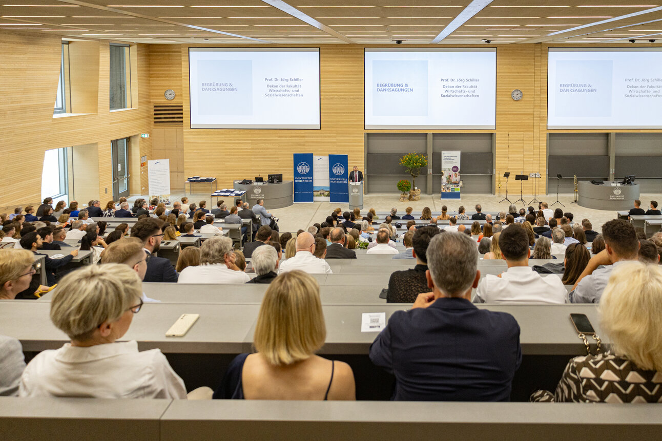 Foto: Ein Hörsaal der Universität Hohenheim ist gefüllt mit Personen, die einer Präsentation von Prof. Dr. Jörg Schiller zuhören. Auf der Leinwand steht 'Begrüßung & Danksagungen'.